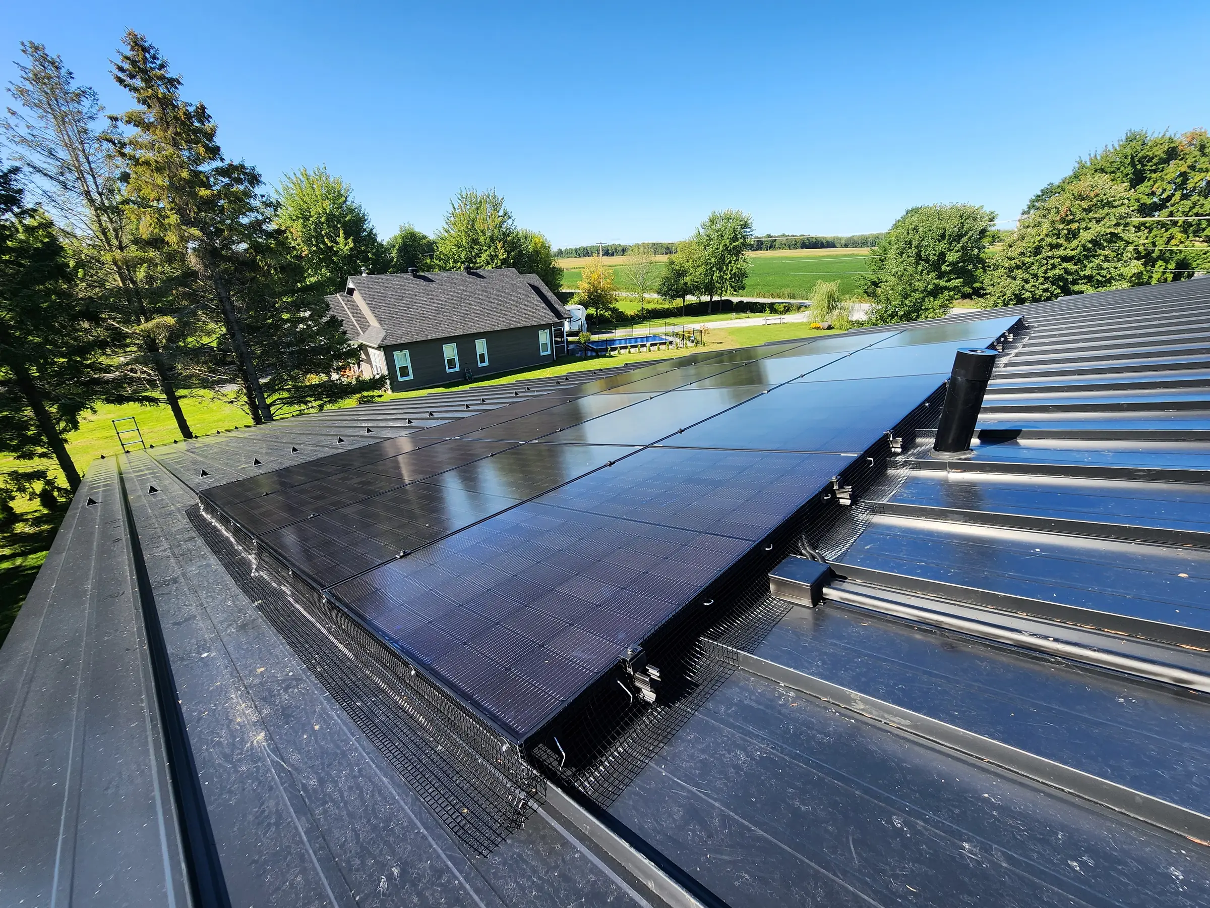 Panneaux solaires noirs installés par Phidel sur une toiture d'acier, champs agricoles en arrière-plan